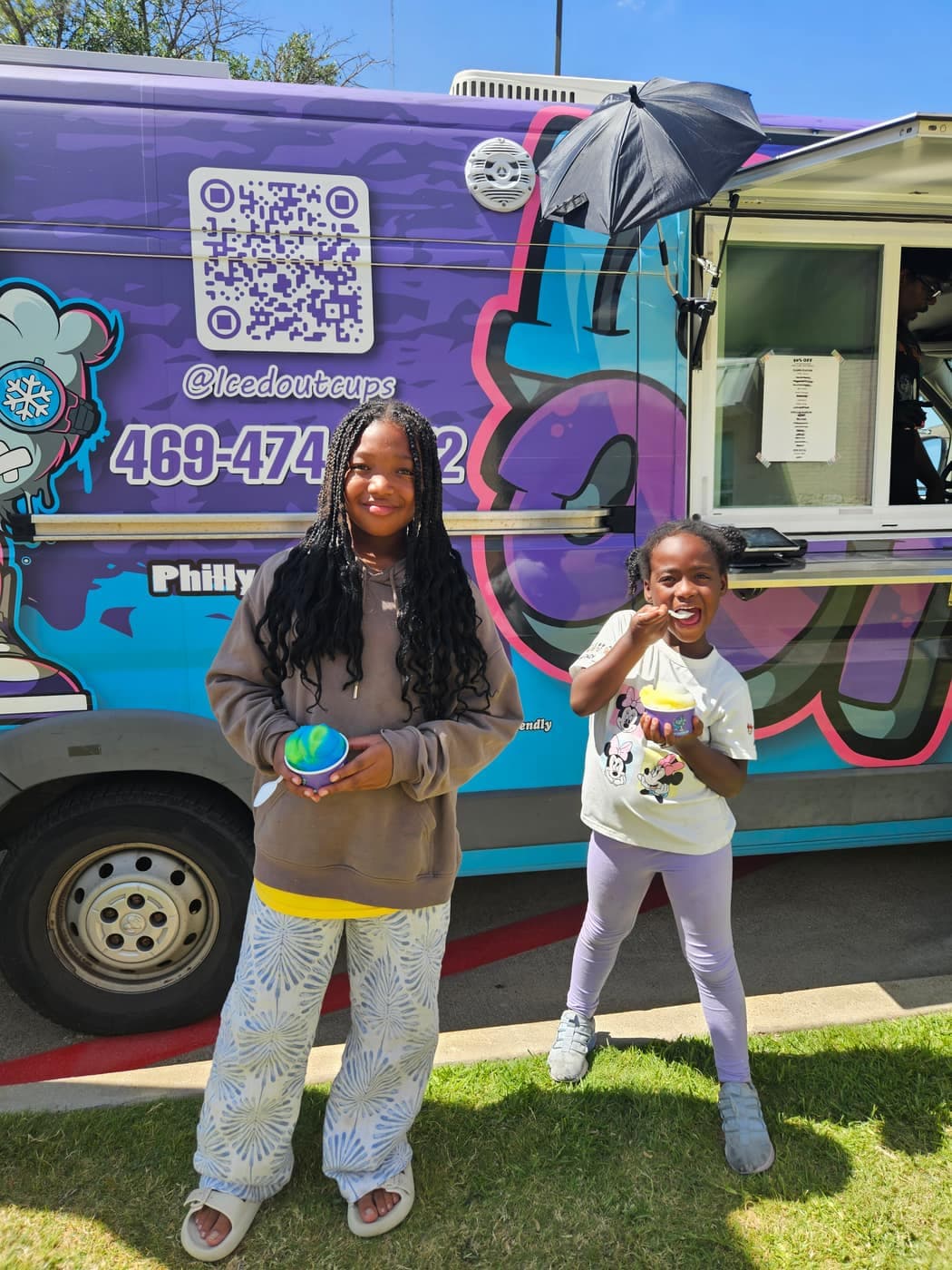 A cup of Iced Out Philly water ice held in front of the purple Iced Out truck