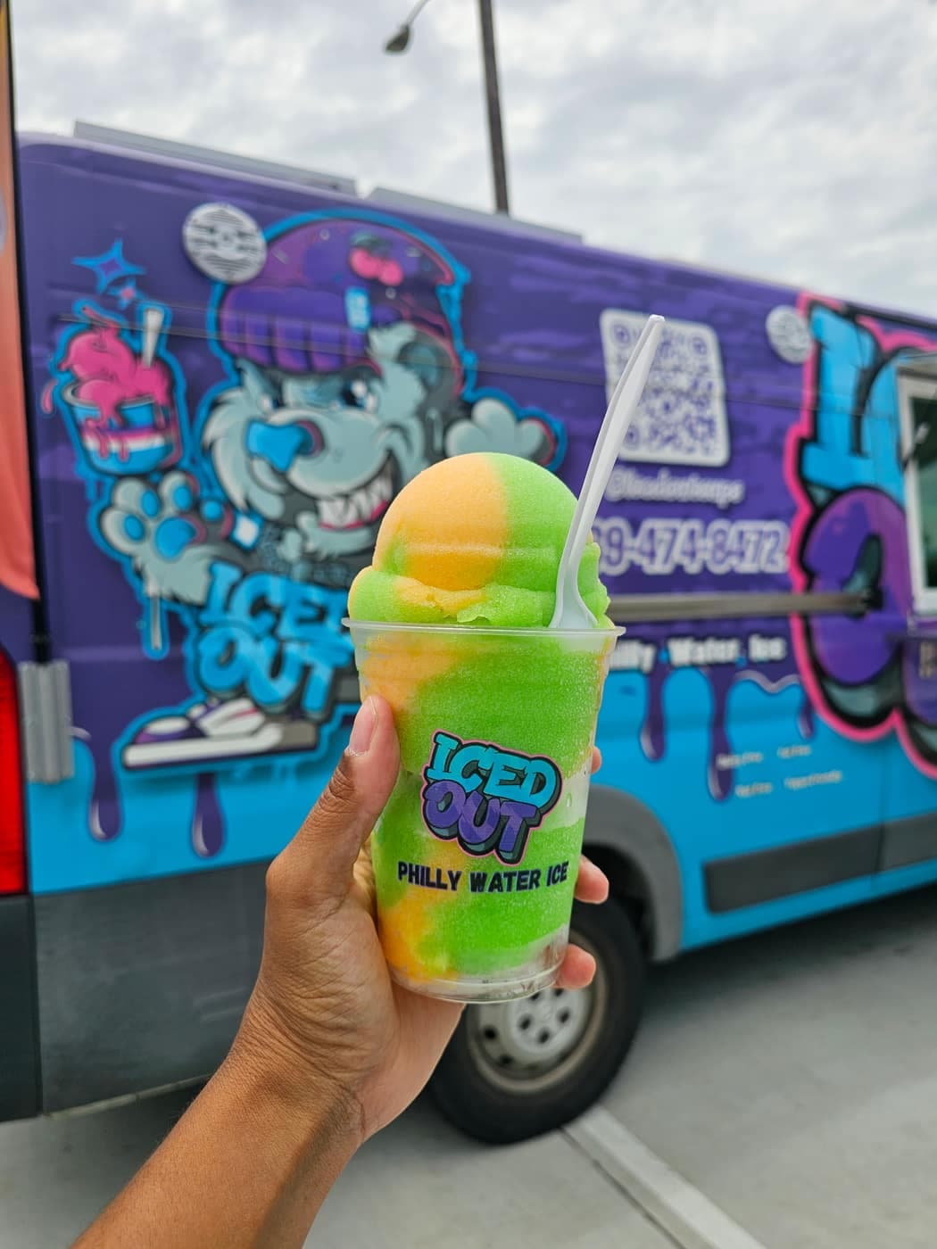 A branded Iced Out cup held up in front of the graffiti-wrapped truck