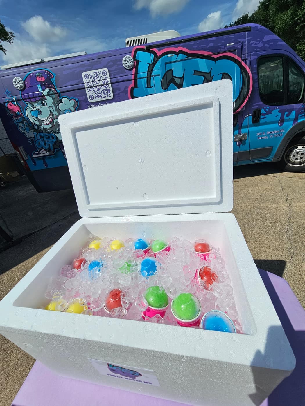 Open foam cooler full of colorful pre-scooped Iced Out cups on ice beside the branded truck